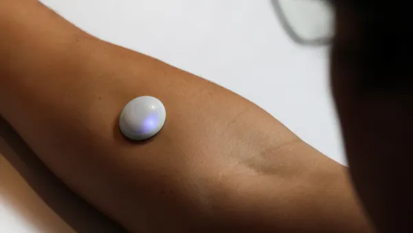 A person wears a small, white round sensor on their forearm.