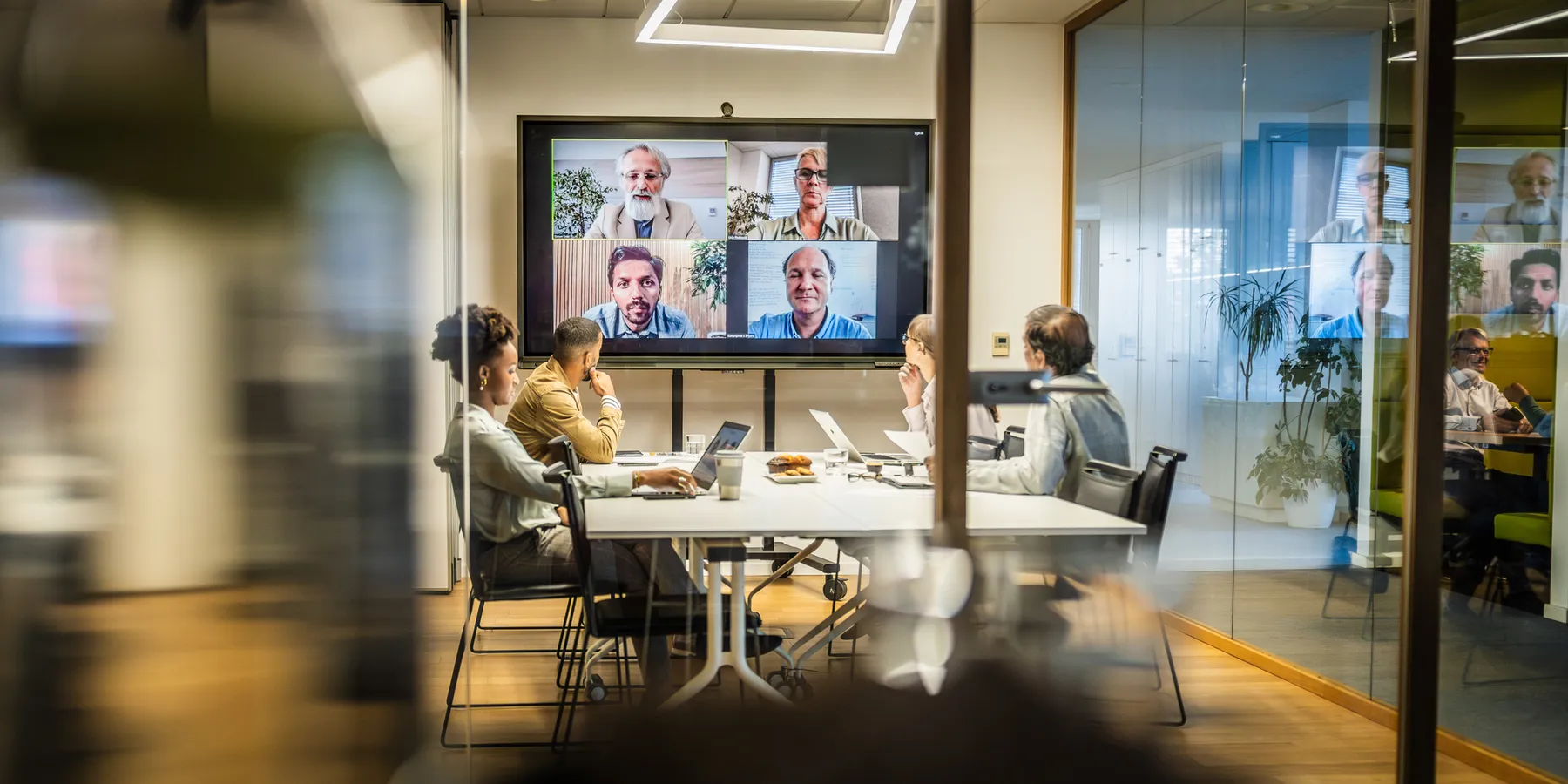 A group of employees attend a hybrid attendance presentation from a small meeting room.