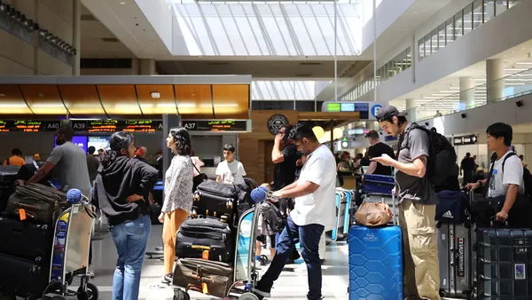 Travelers wait in line at an airport check-in counter.