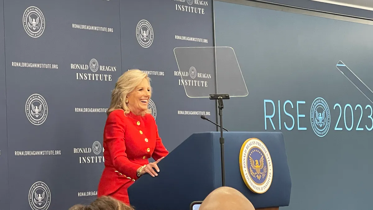 First Lady Jill Biden speaks at a podium wearing a red pantsuit.