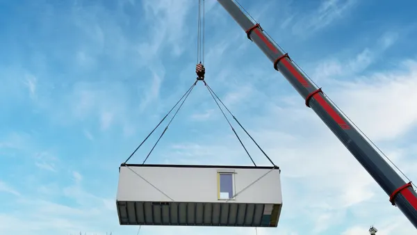 A modular building unit is lifted by a crane.
