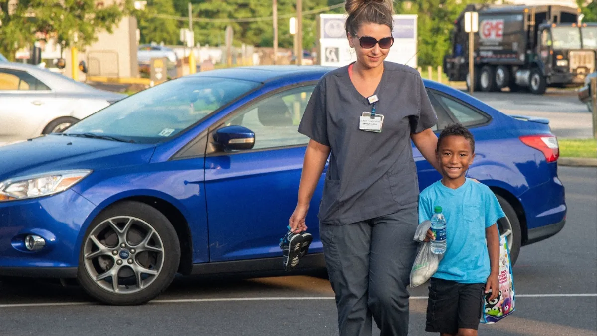 An adult guiding a child walking in a parking lot