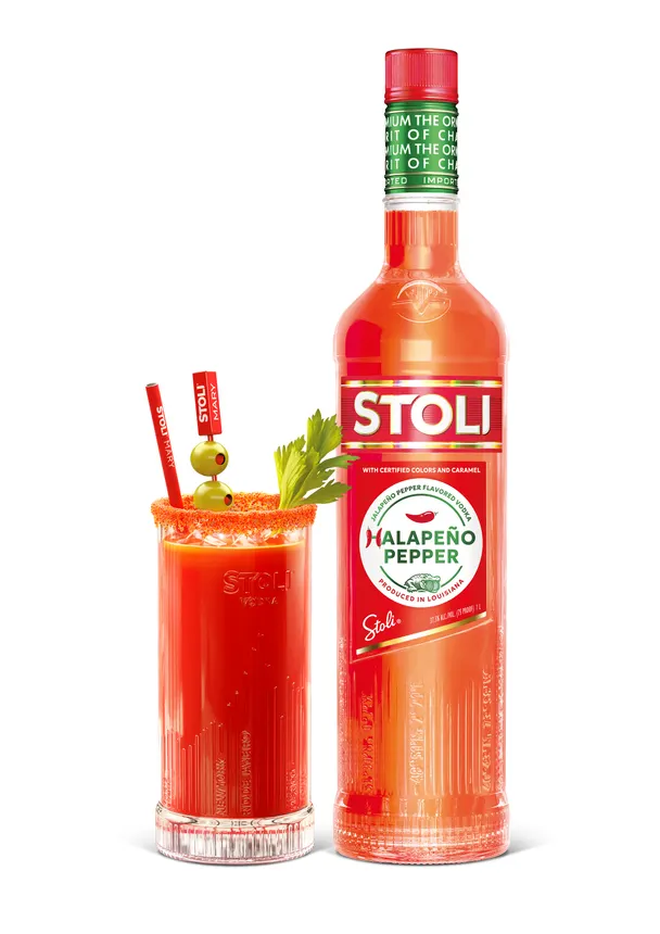 A mixed Blood Mary Cocktail in a glass with a celery and olive garnish next to a Stoli vodka bottle.