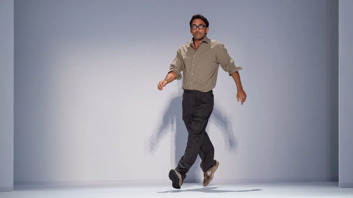 A person strides down the runway as an audience applauds from the sidelines.