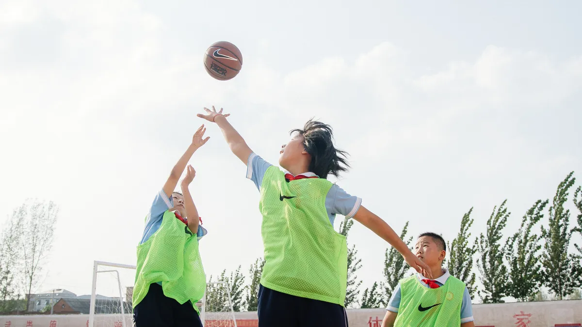 Three students play basketball on a Nike Grind court.