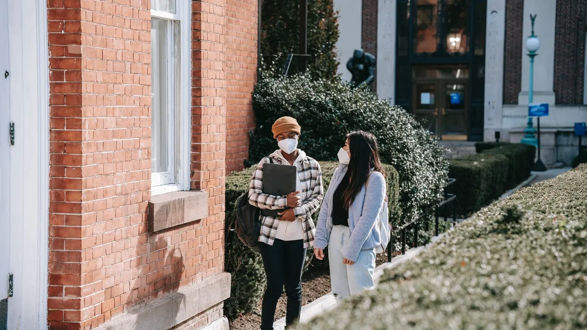 two college students walk on campus while wearing facemasks