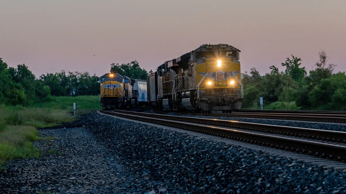 Two freight trains with yellow locomotives are seen on rail tracks.