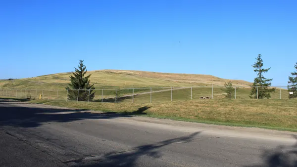 Image of a large mound covered in grass taken from a road.