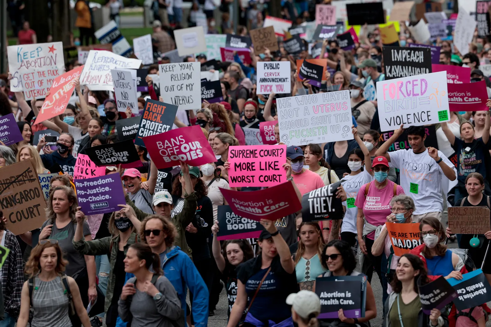 A large group of protestors gather on the street. Some signs read "bans off our bodies", "Forced birth = violence", and "fight back. protect choice."