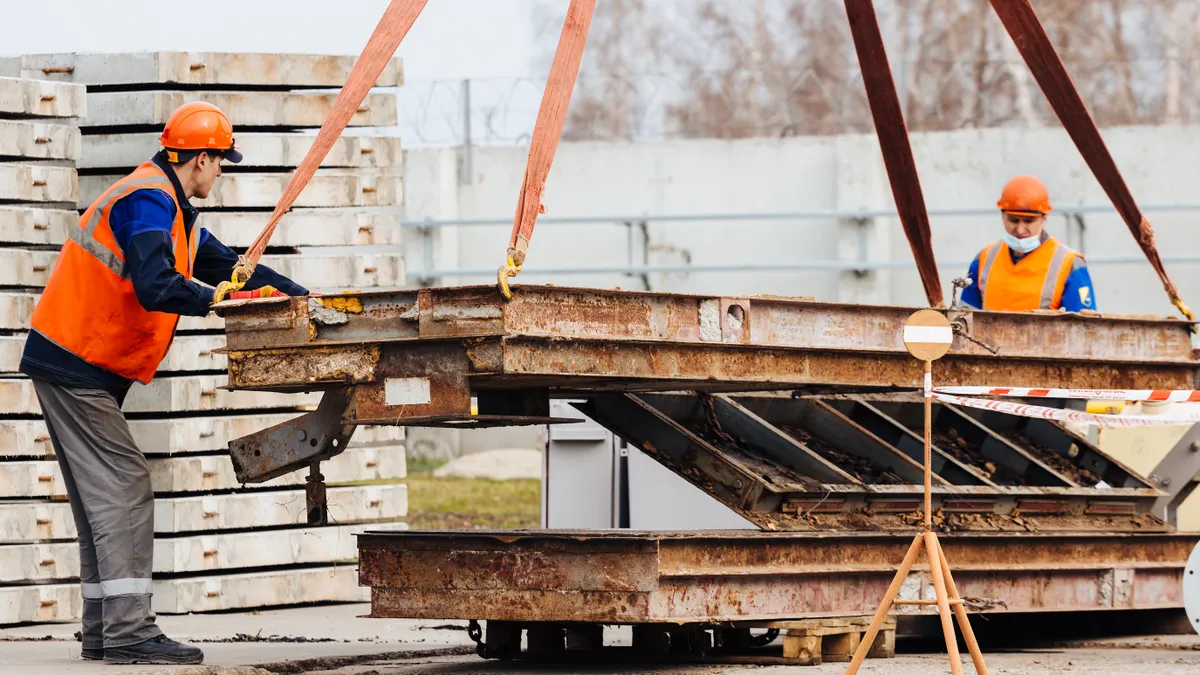 Slinger in helmet and vest controls unloading of metal structures on construction site.