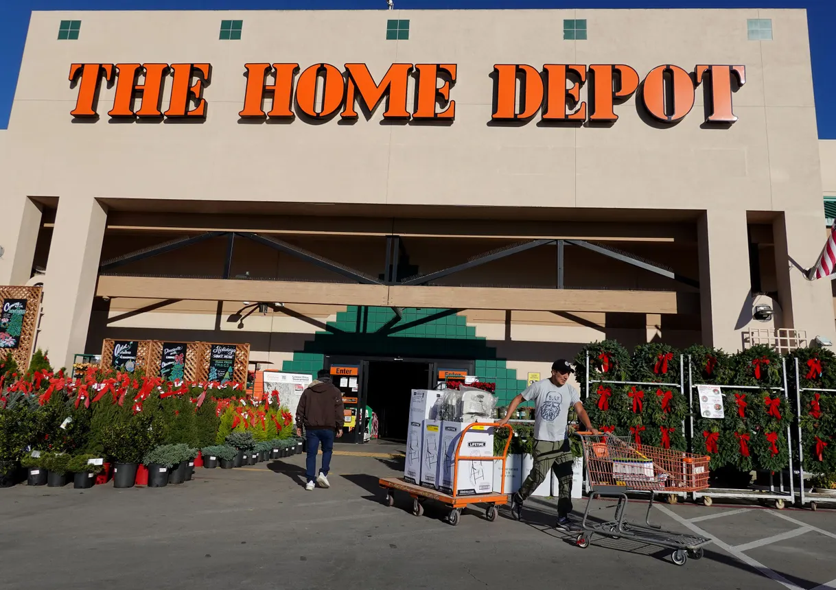 A person pulls a car with products on it out of a Home Depot retail store while another walks in.
