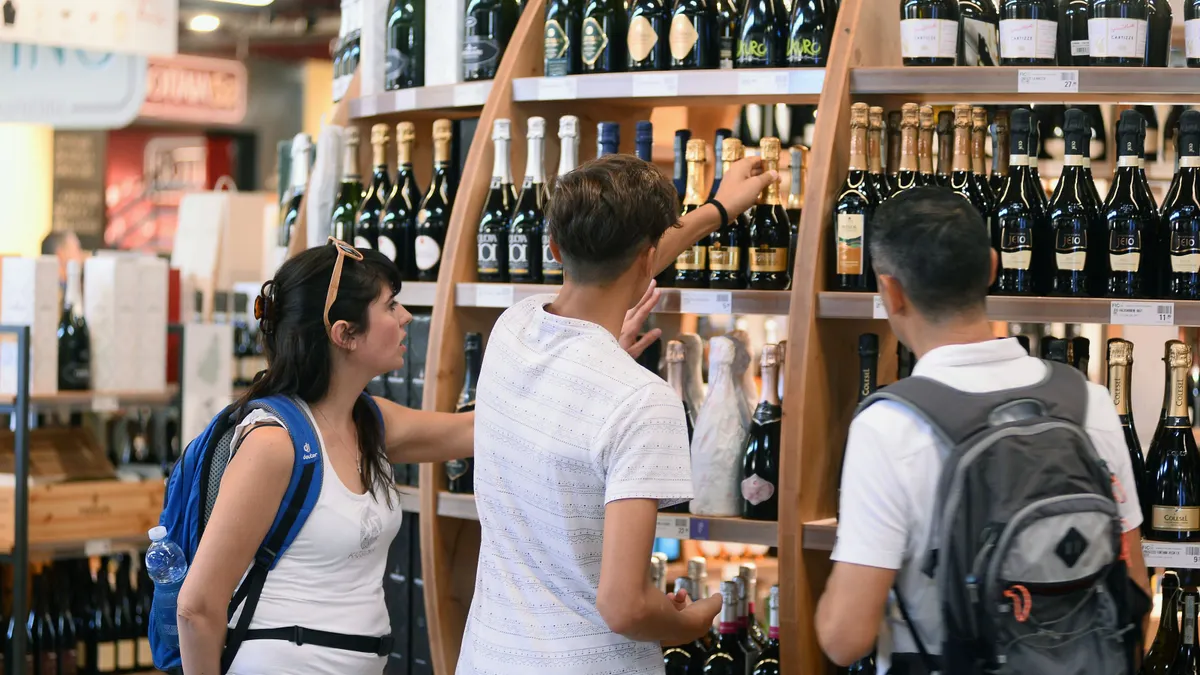 Three people browse a wine aisle.