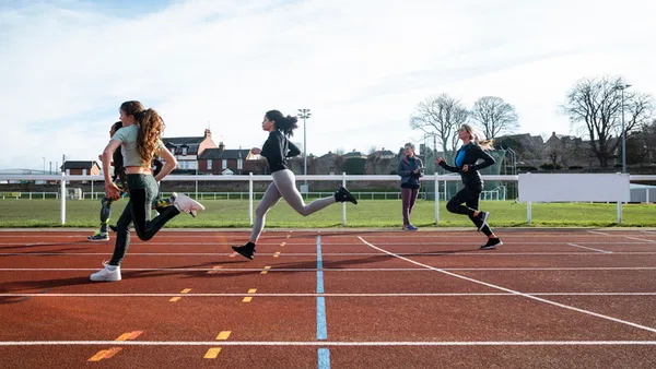 a handful of people are running outside on a track near a sports field.