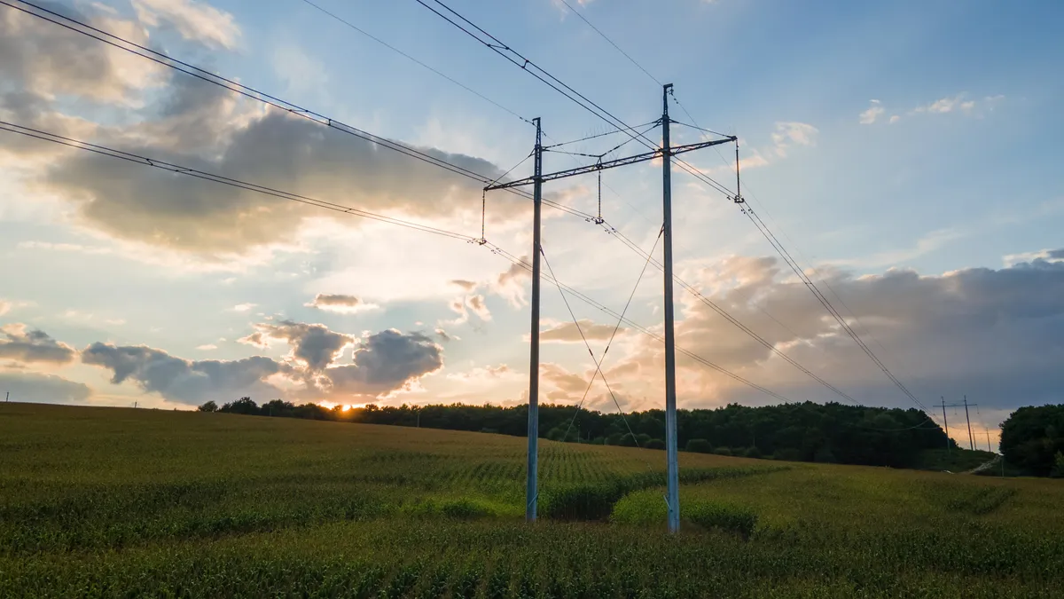 Tower with electric power lines for transfering high voltage electricity located in agricultural cornfield.