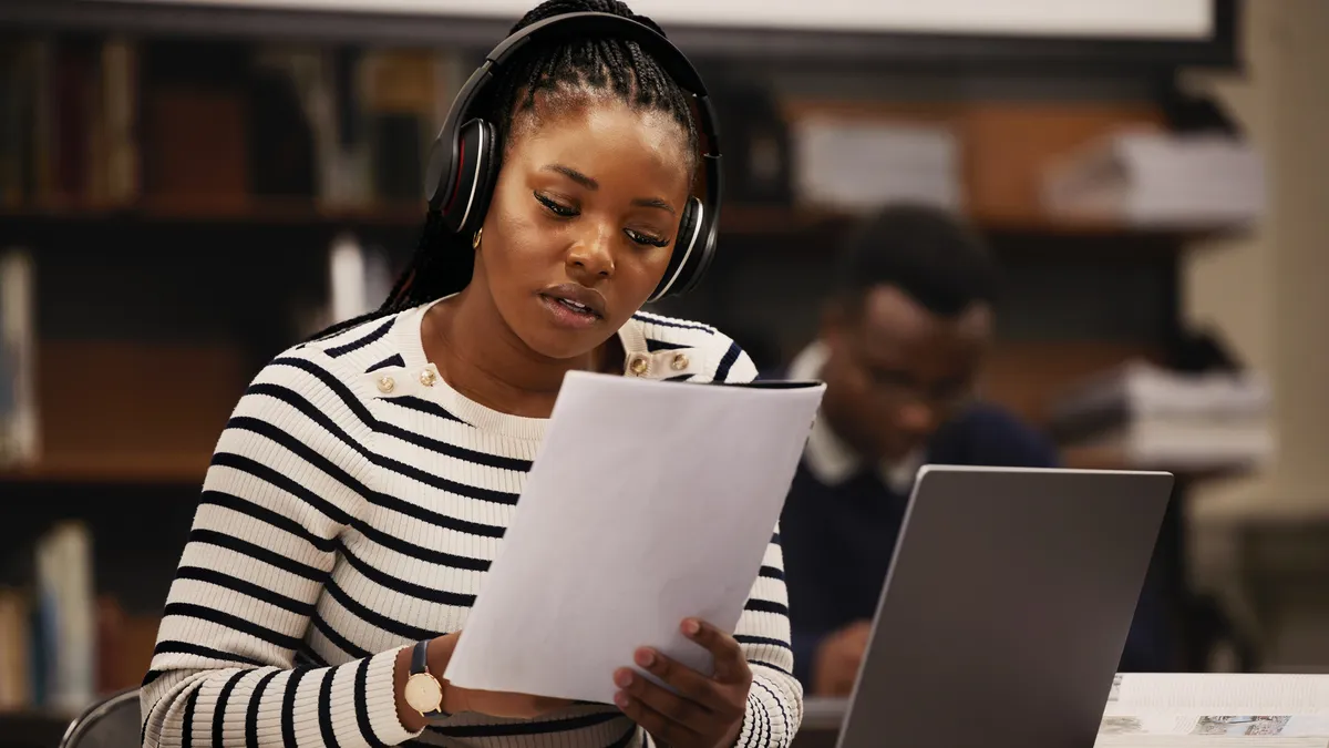 A college student listens to music while reading a paper.