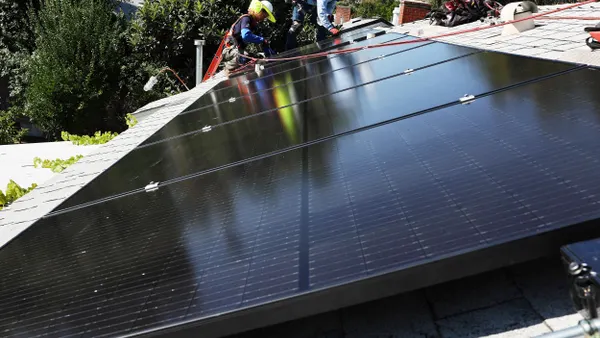 Workers install solar panels on the rooftop of a house