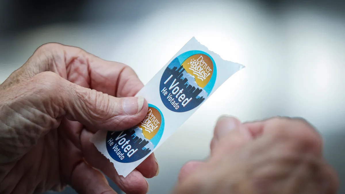 An election judge tears off a couple of "I Voted" stickers to hand to a voter as people cast their ballots in the State Primaries on June 28, 2022 at the Wellington E. Webb Municipal Office Building i