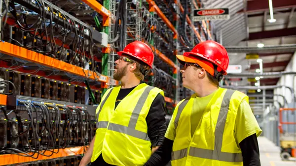 Two men walk in front of electrical equipment.