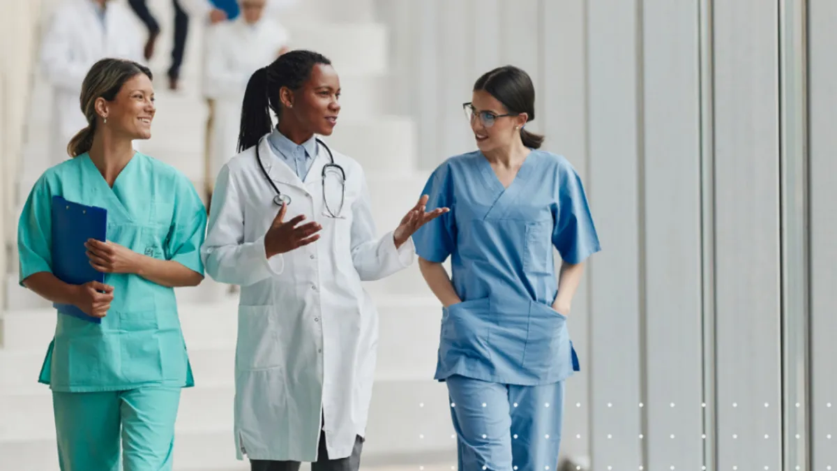 Three medical care workers talking and walking down a hallway.