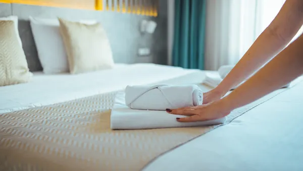 Hands place fresh towels on a hotel bed.