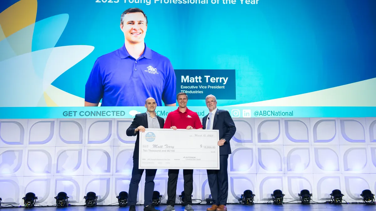 Three people on a stage pose with a large prize check.