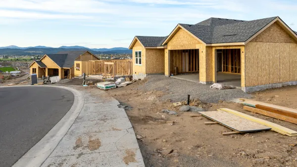 Wood frames for homes under construction surrounded by dirt with a concrete road in the foreground.