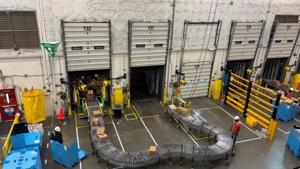 Boxes are being unloaded from a truck onto a conveyor belt with employees working in the background.