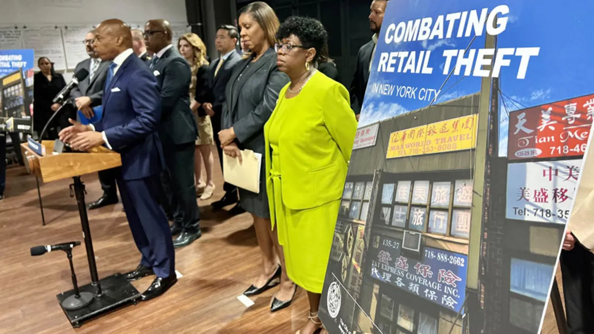 A person speaks at a microphone, surrounded by a group of people. A sign on the right says "Combating retail theft New York City."