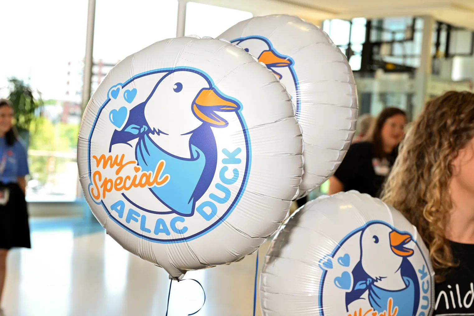 A woman holds balloons featuring the Aflac duck.