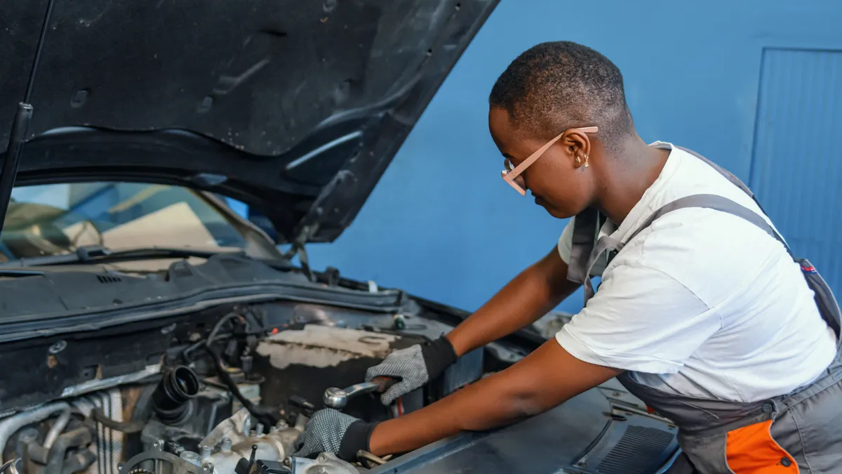 An African-American person is using a wrench to repair a broken car