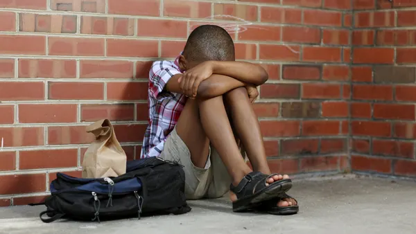 Young boy sitting alone with head buried against a brick wall