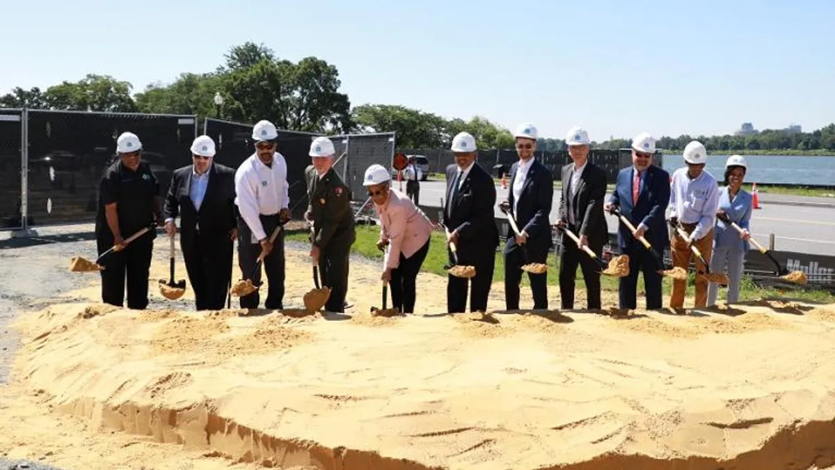 People in suits and white helmets hold shovels of dirt.