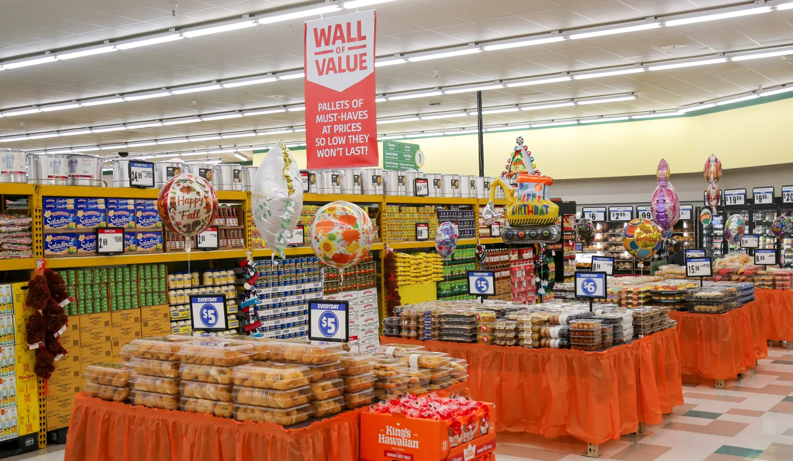 Food on shelves and tables in a grocery store beneath a sign that reads "Wall of Value."