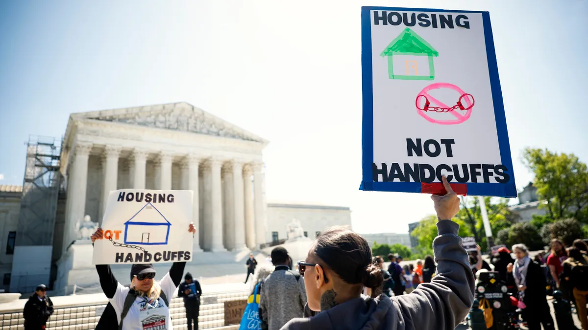 People hold signs that read "Housing not handcuffs" in front of a courthouse.