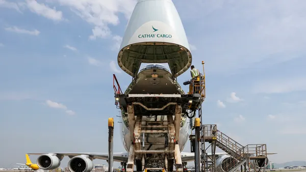 The nose of a Cathay Pacific cargo freighter is open with a cargo handler loading the aircraft.