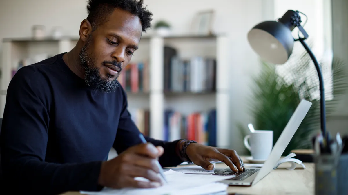 Man working at home on computer with pen.