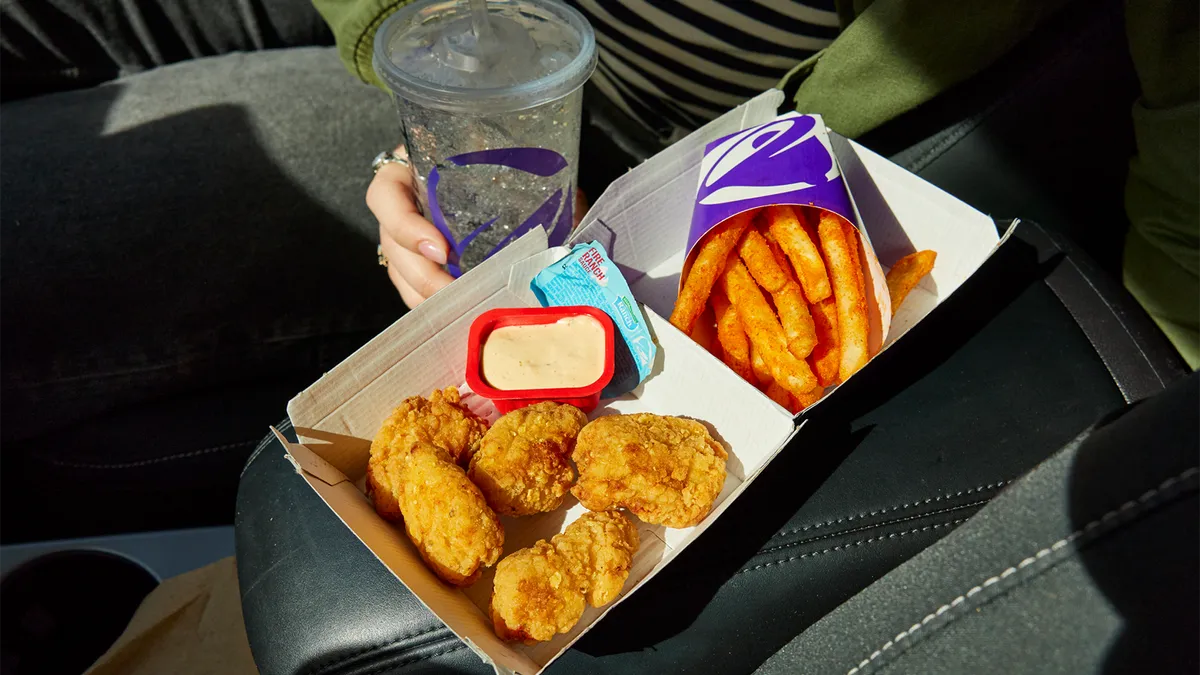 A person holding an order of Taco Bell chicken nuggets, nacho fries and a drink.