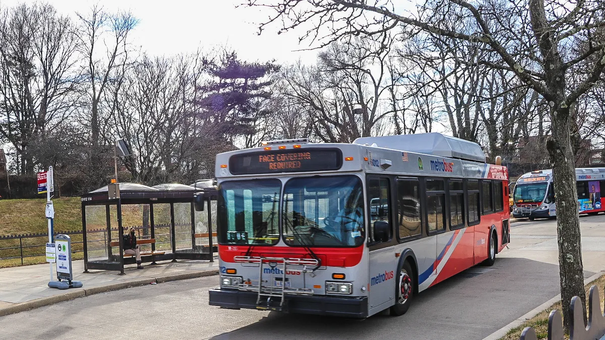 A Washington Metropolitan Area Transit Authority bus drives along a lane by a bus stop.