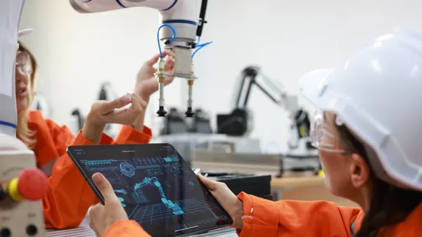 Two engineers work with a tablet to fix a robotic arm in a factory.
