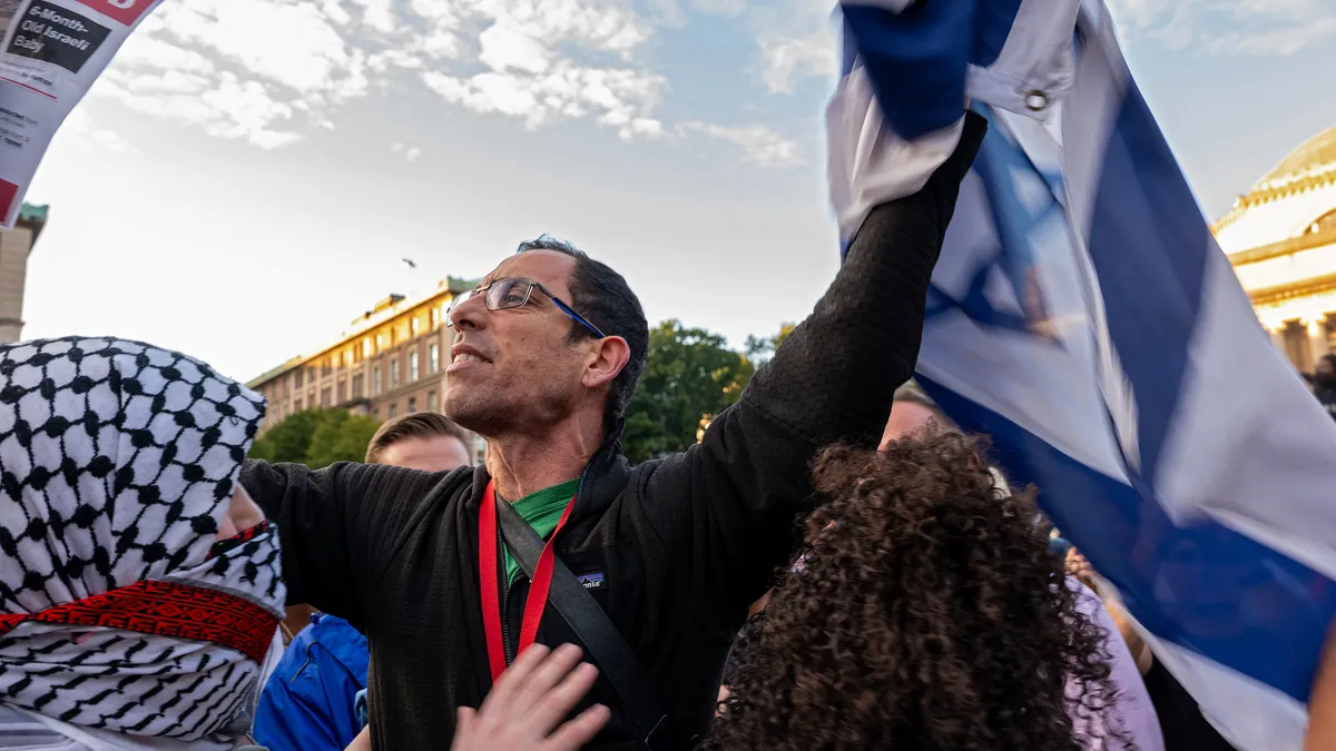 A man holds up an Israeli flag in front of a woman wearing a kufiyya