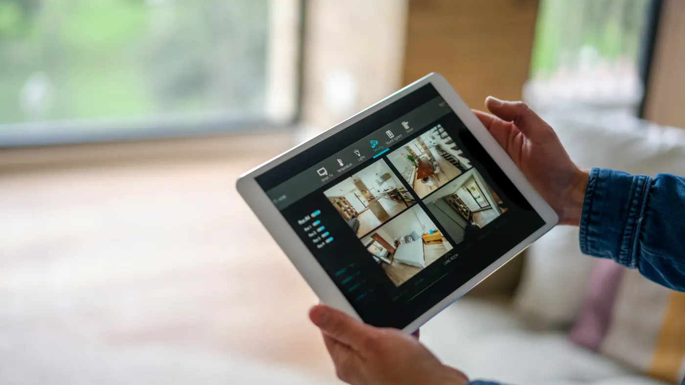 Close-up on a woman monitoring all the rooms in her house with a home security system using a digital tablet.