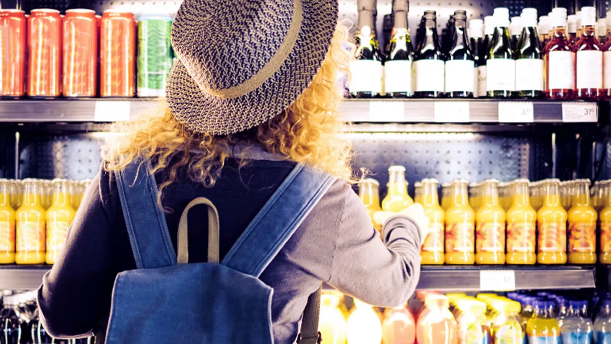 Person viewed from back choosing beverage from refrigerated shelves