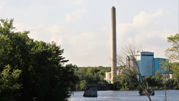 An industrial facility with a tall smokestack sits on the far shore of a creek.