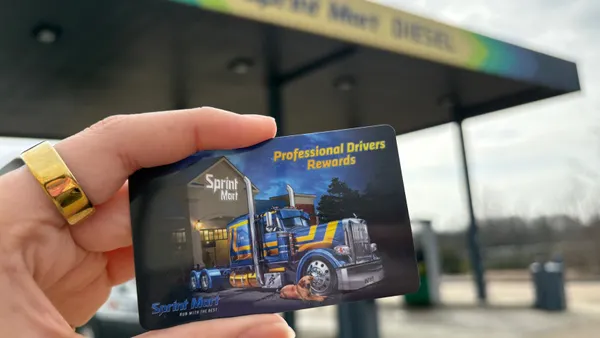 A photo of a hand holding a card in front of a fuel canopy. The card says Sprint Mart professional drivers rewards.