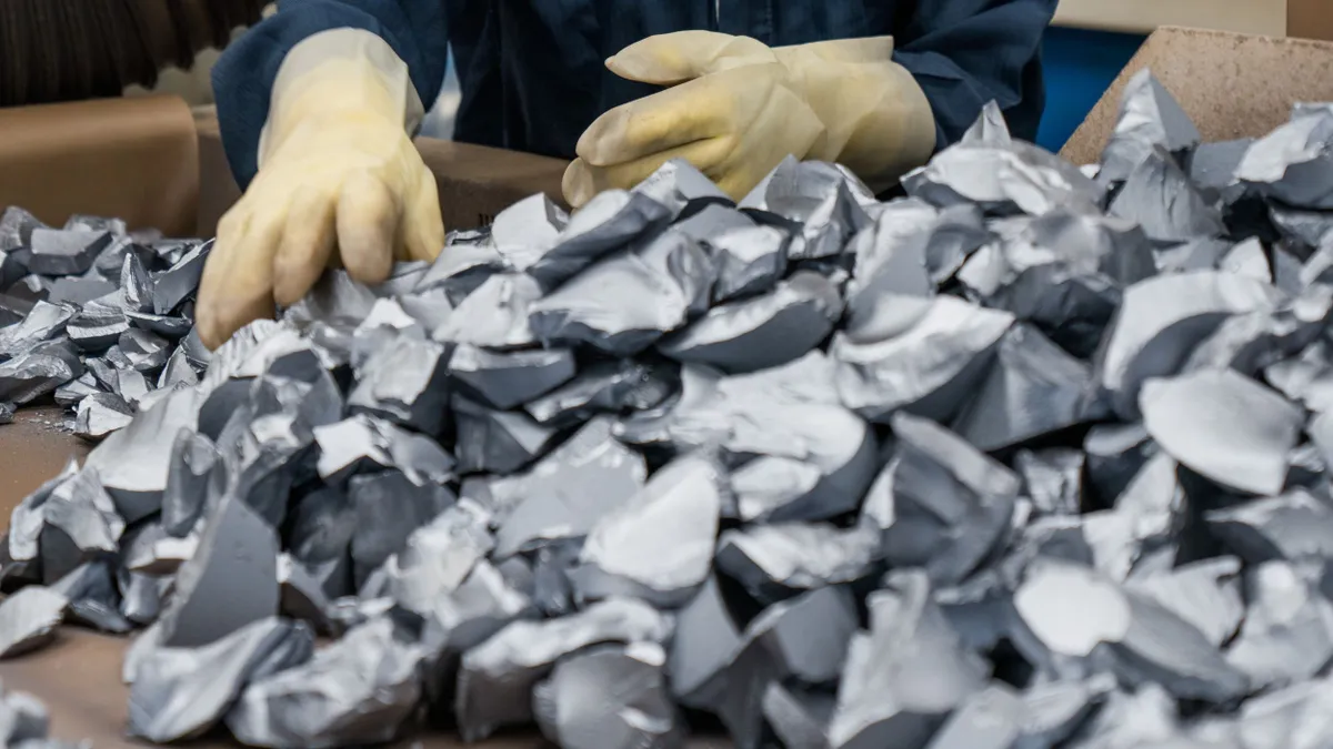 A person with gloves handling a pile of raw silver materials.