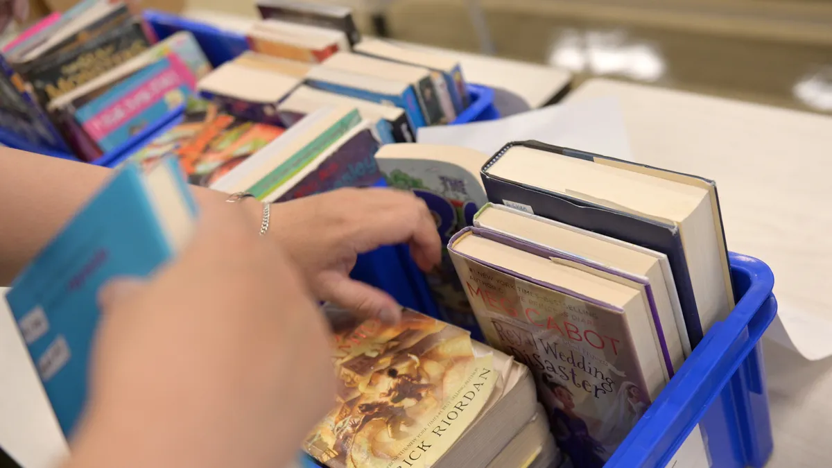 An educator's hands are shown organizing library books in blue bins following their collection from students.