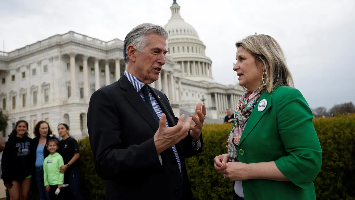 A man speaks with a woman with the U.S. Capitol building in the background.