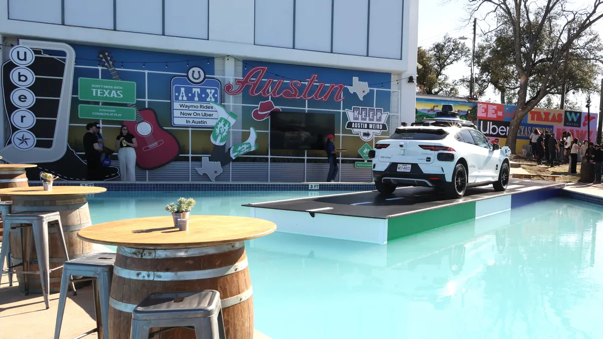 A white car on a platform in front of a building with signs reading "Austin," "Texas" and "Uber."