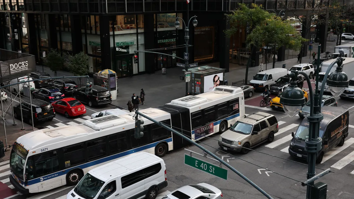 Overhead view of a busy city intersection with an articulated bus and many cars.