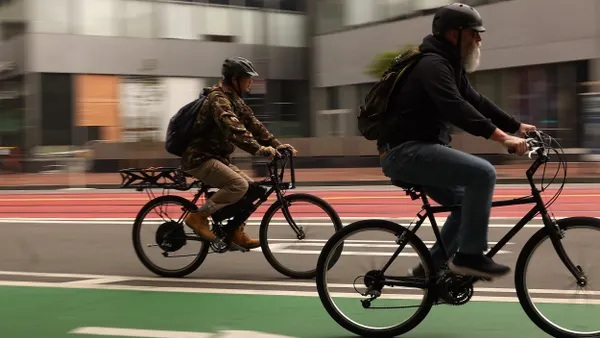 Two electric bikes with riders on a street pavement.